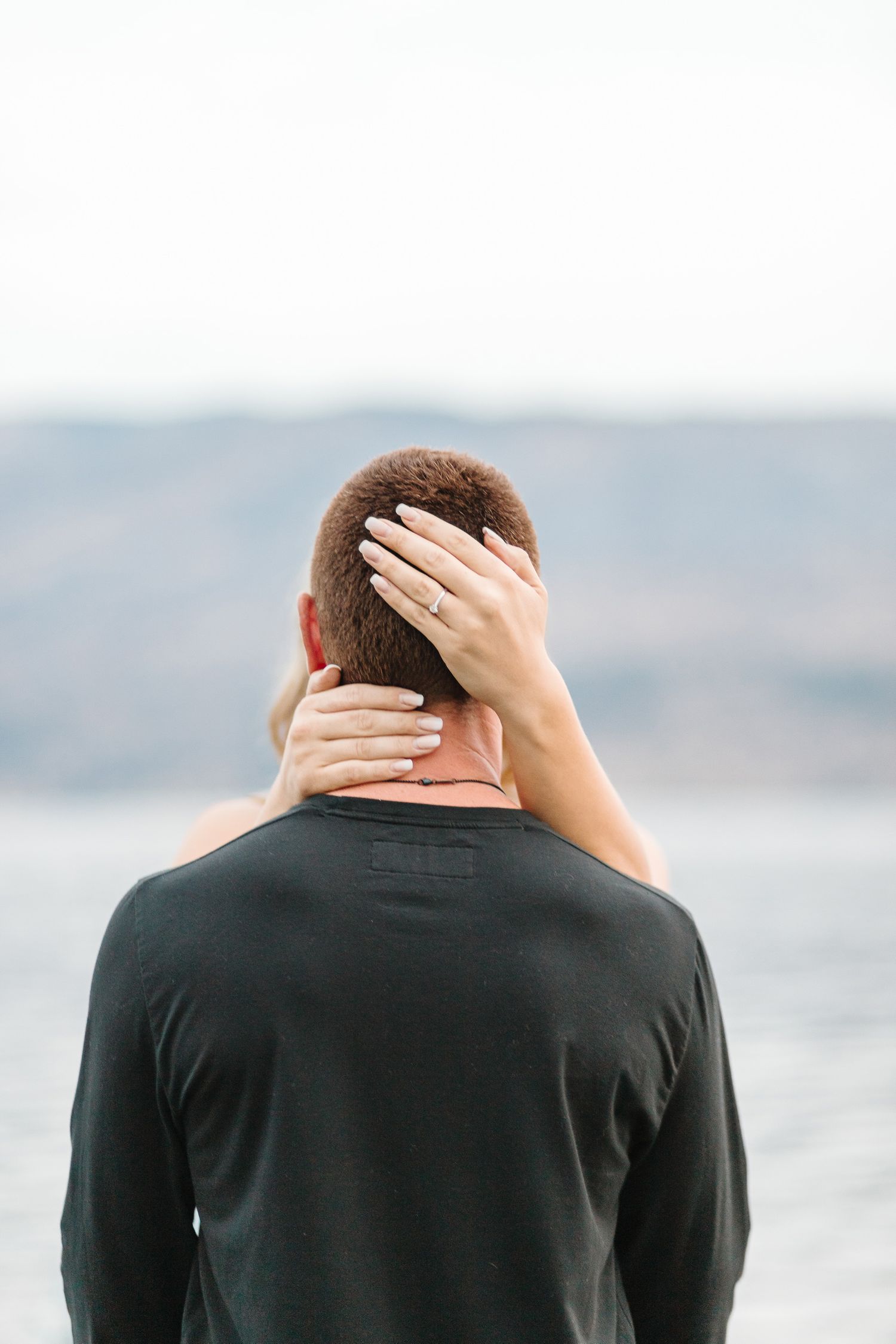 Close-up view of couple embracing with lake and mountains in background.