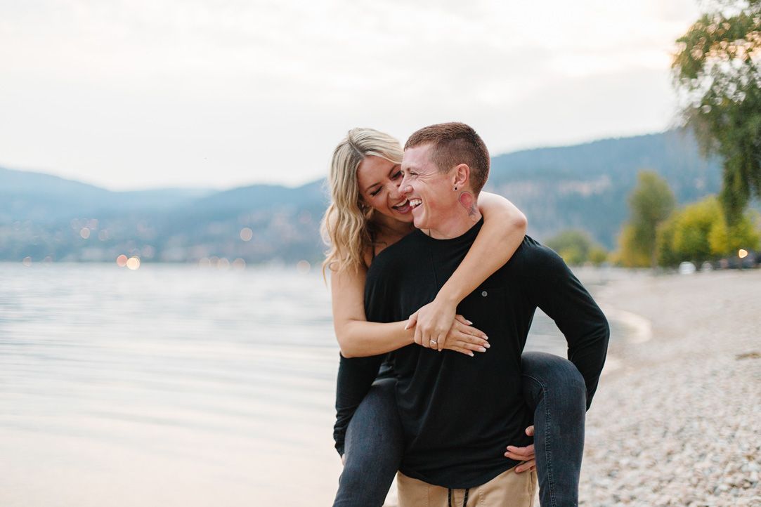 Romantic couple poses together by scenic lake with mountains in background.