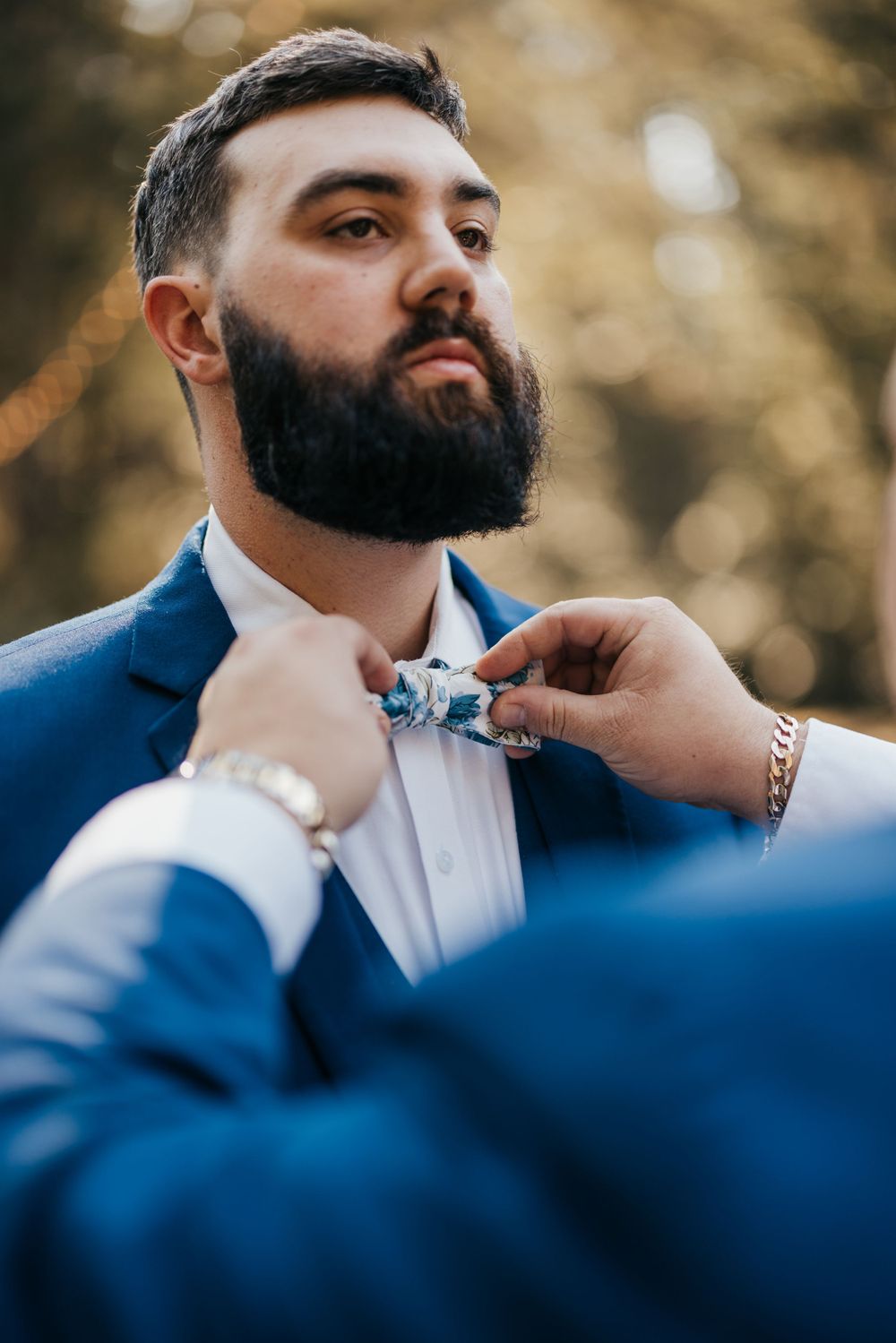 Close-up of bow tie being adjusted on formal blue suit.