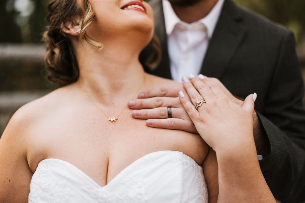 Close up shot of a wedding ring and hands against a white wedding dress bodice.
