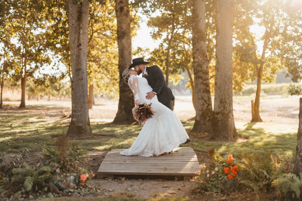 Romantic wedding couple dancing in golden sunlight between trees on wooden platform.