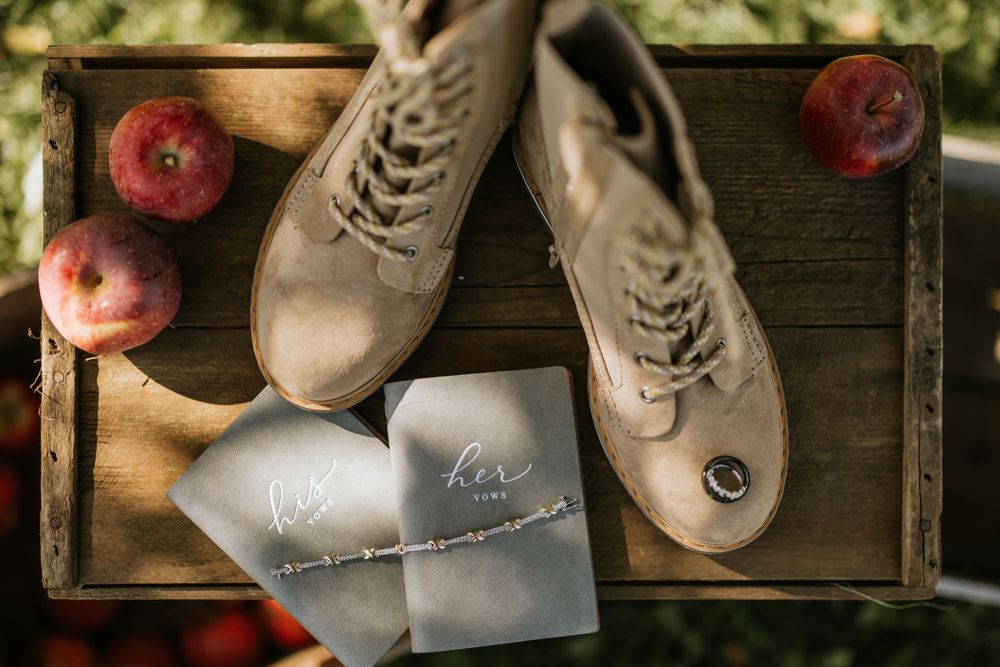 Wedding shoes and invitations arranged on a wooden tray with red apples creating a rustic composition.