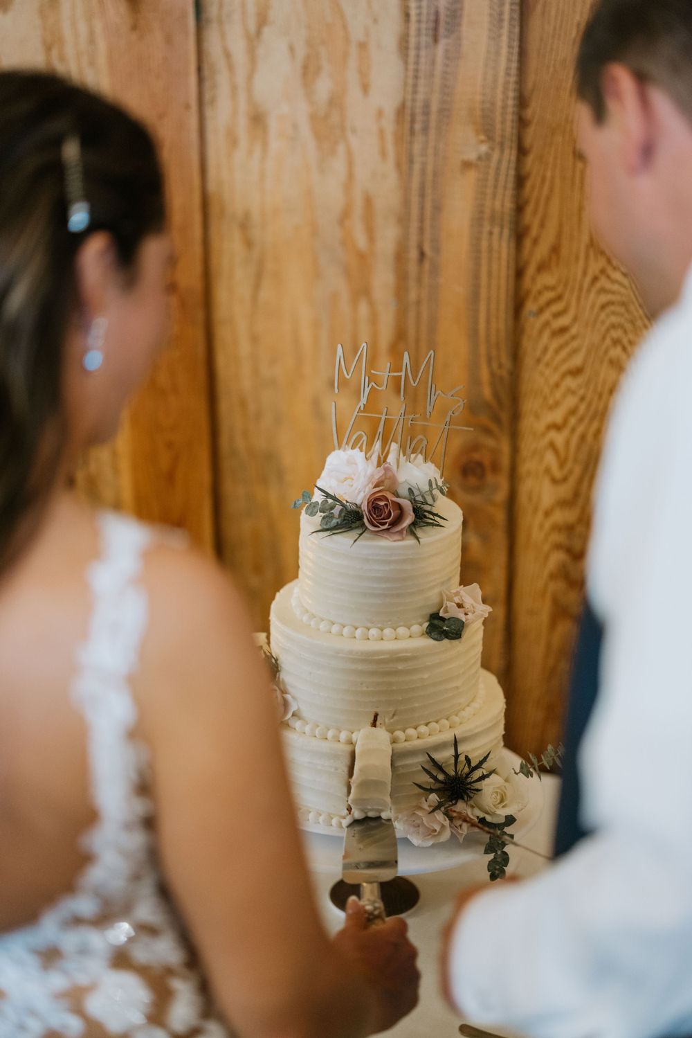 Classic white three-tier wedding cake with floral decorations viewed by couple.