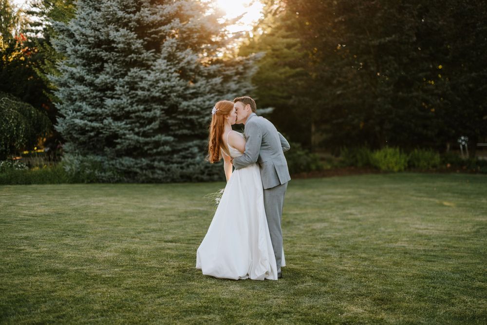 Romantic sunset wedding portrait of couple embracing on manicured lawn with evergreens.