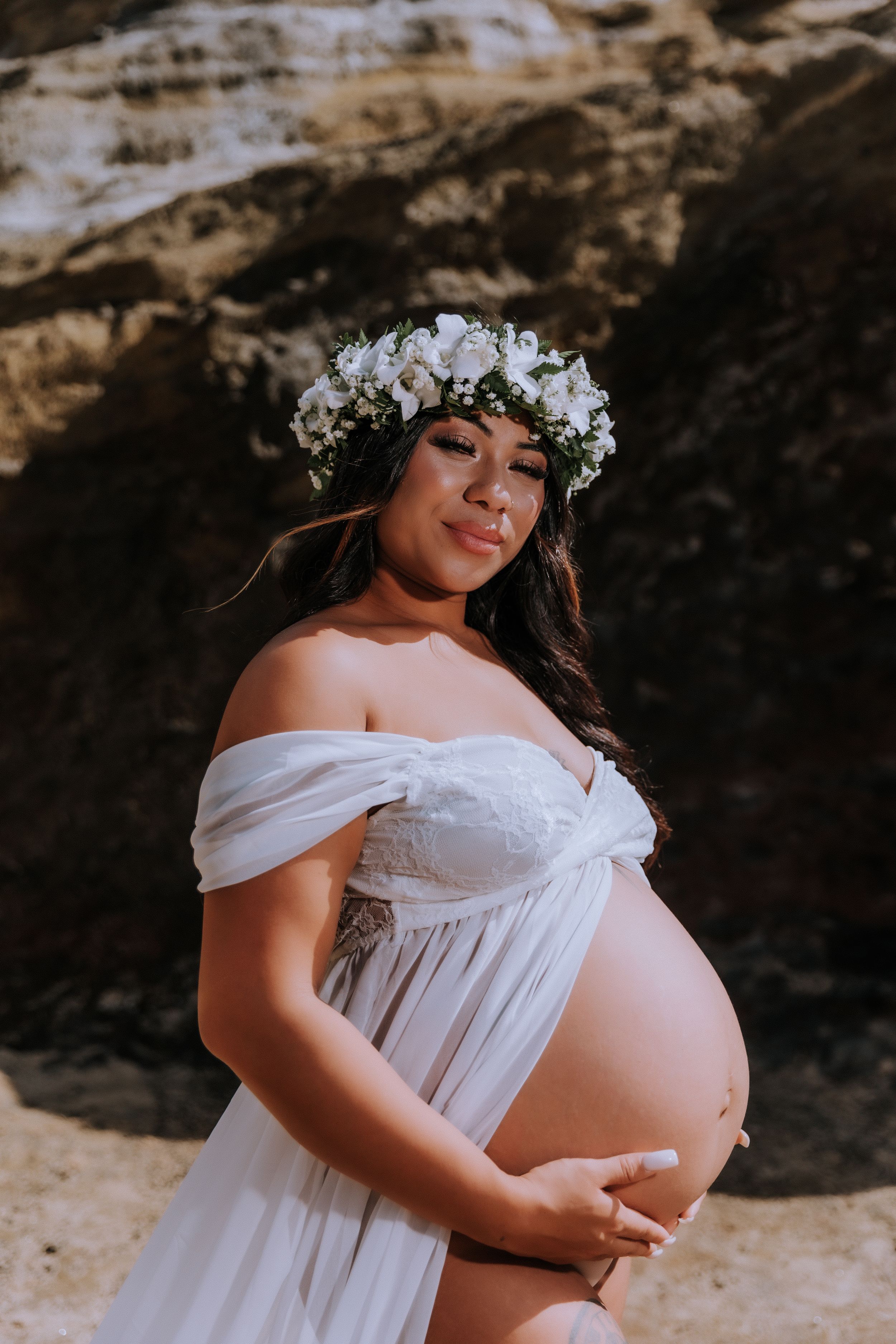 Dreamy beach maternity portrait in white off-shoulder dress with flower crown.
