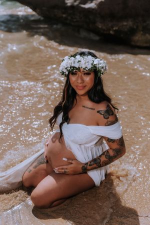 Beachside photography session with woman in white dress and flower crown posing on wet sand.