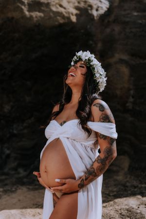 Joyful maternity moment captured against dark rocky beach backdrop.