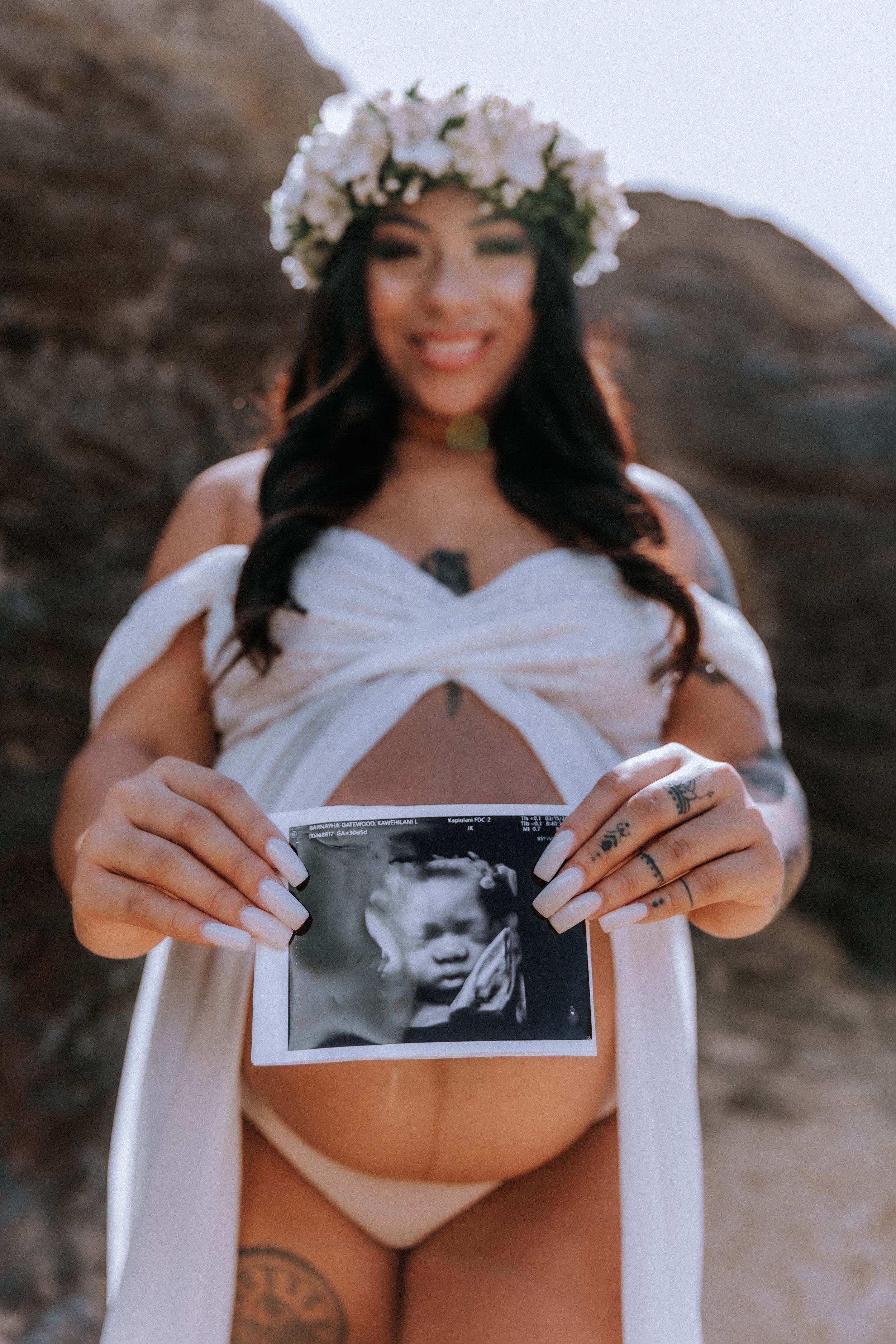 Maternity photo session with ultrasound pictures on rocky beach.