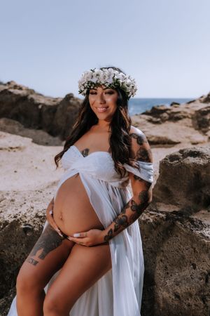 Artistic maternity photography on beach with white dress and floral crown.