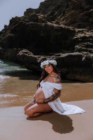 A beach photoshoot featuring a woman in flowing white fabric laying on wet sand near rocky cliffs.