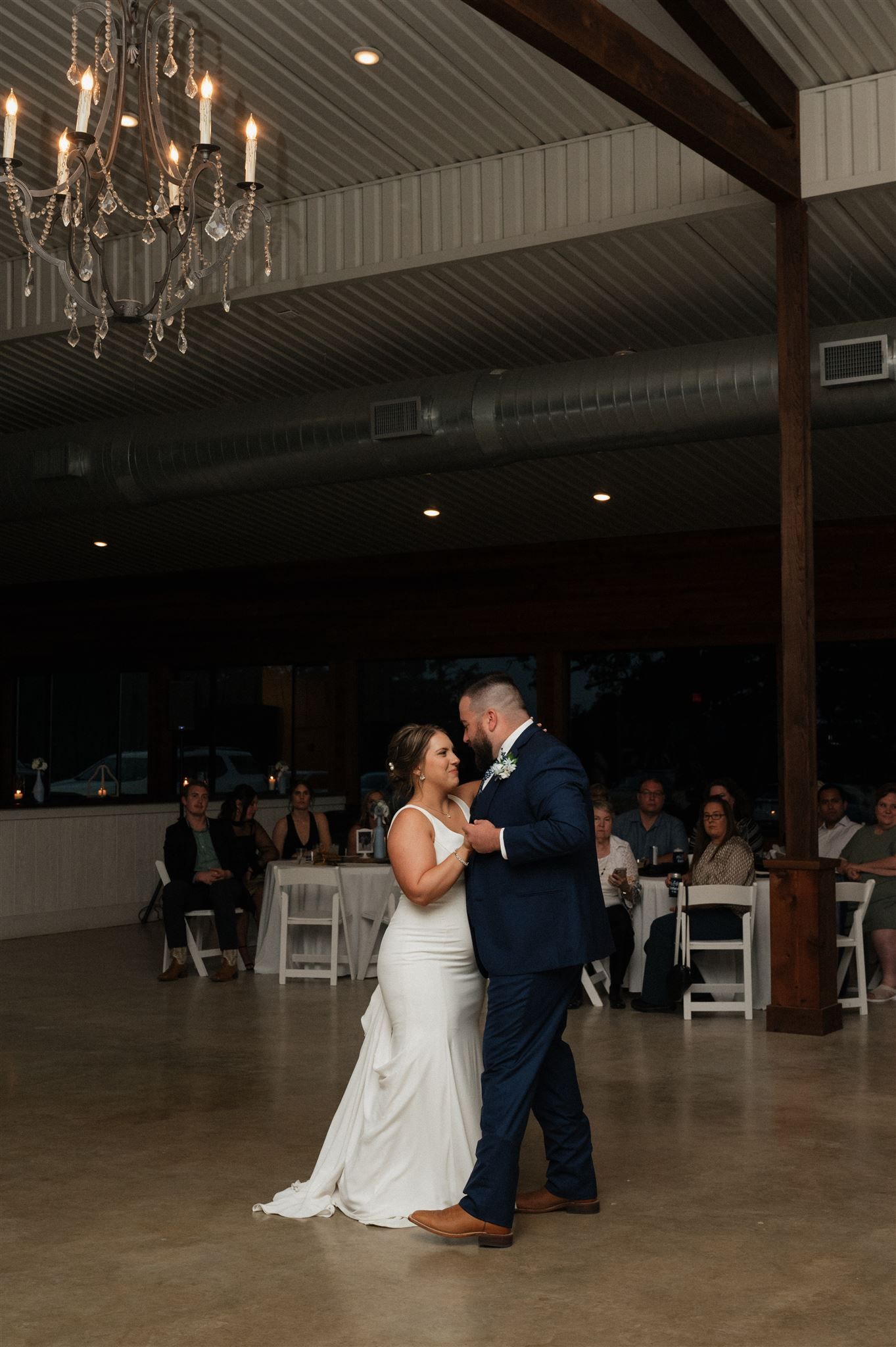 A wedding couple dances in an elegant reception venue with a crystal chandelier overhead.