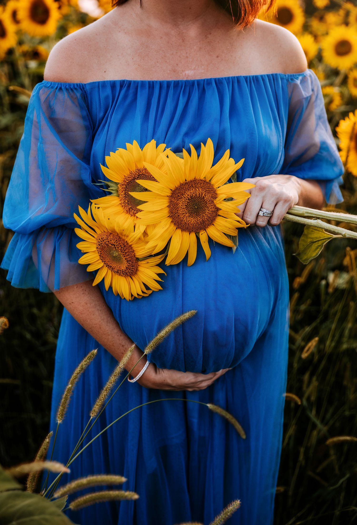 Maternity photo with bright sunflowers against blue off-shoulder dress in sunflower field.