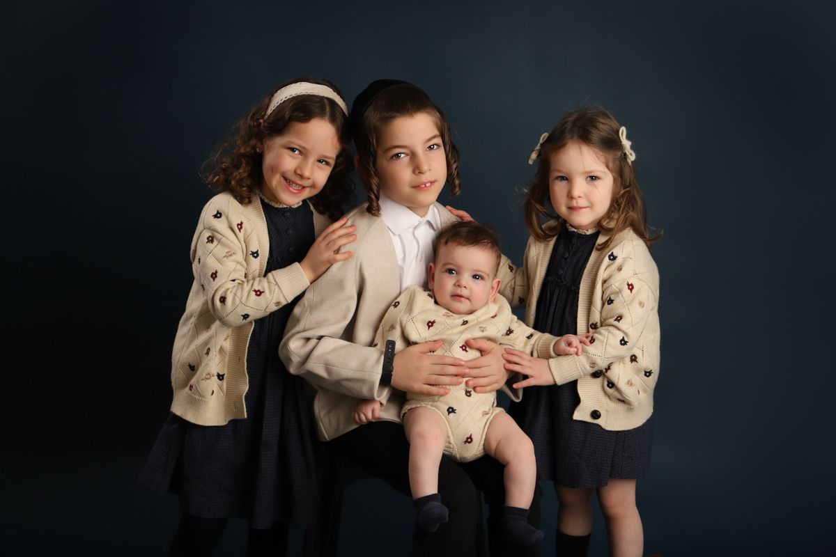 A studio portrait of four siblings wearing matching polka dot sweaters against a dark background.