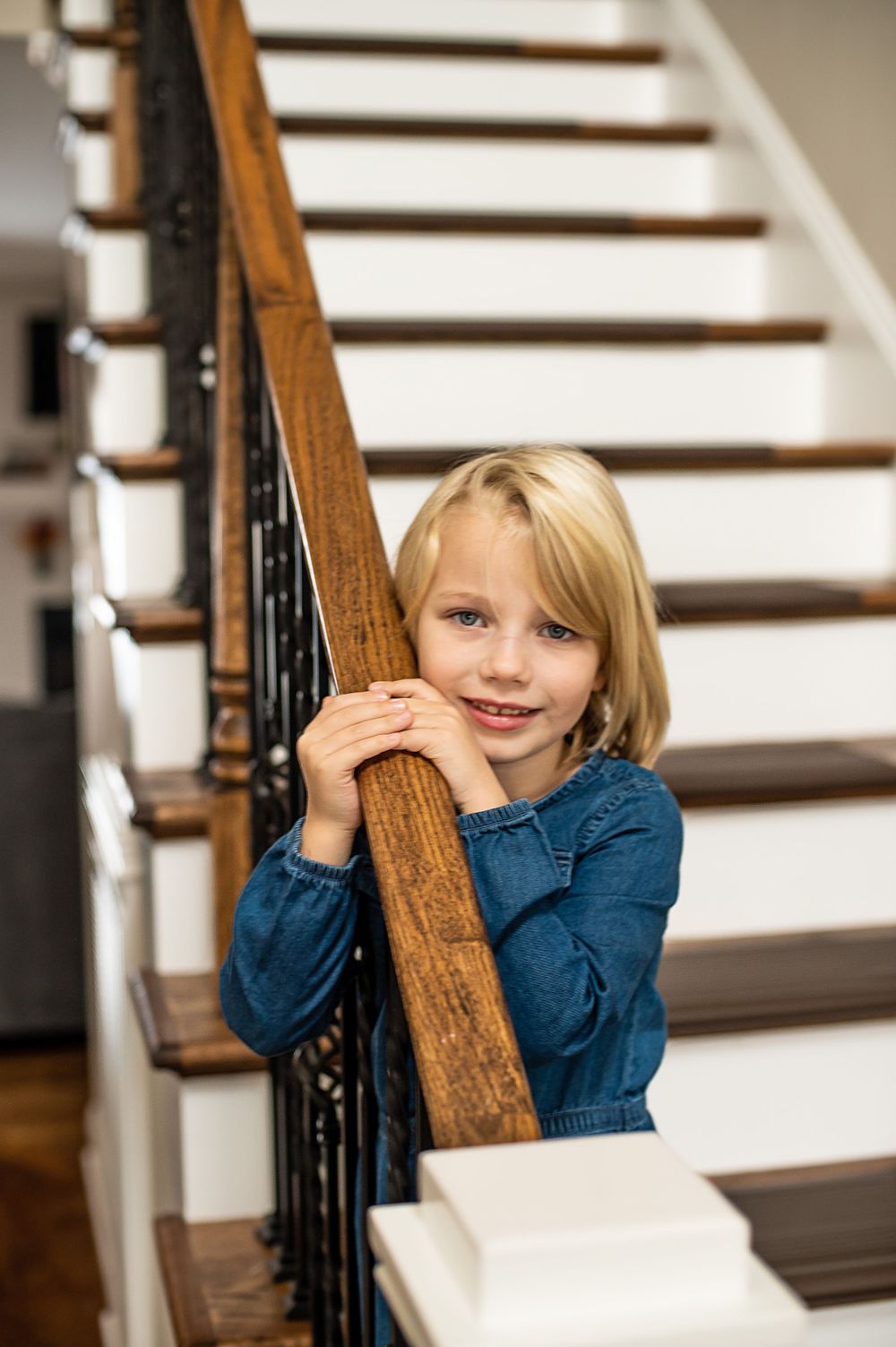 Playful peek around wooden stair banister in sunlit home interior.