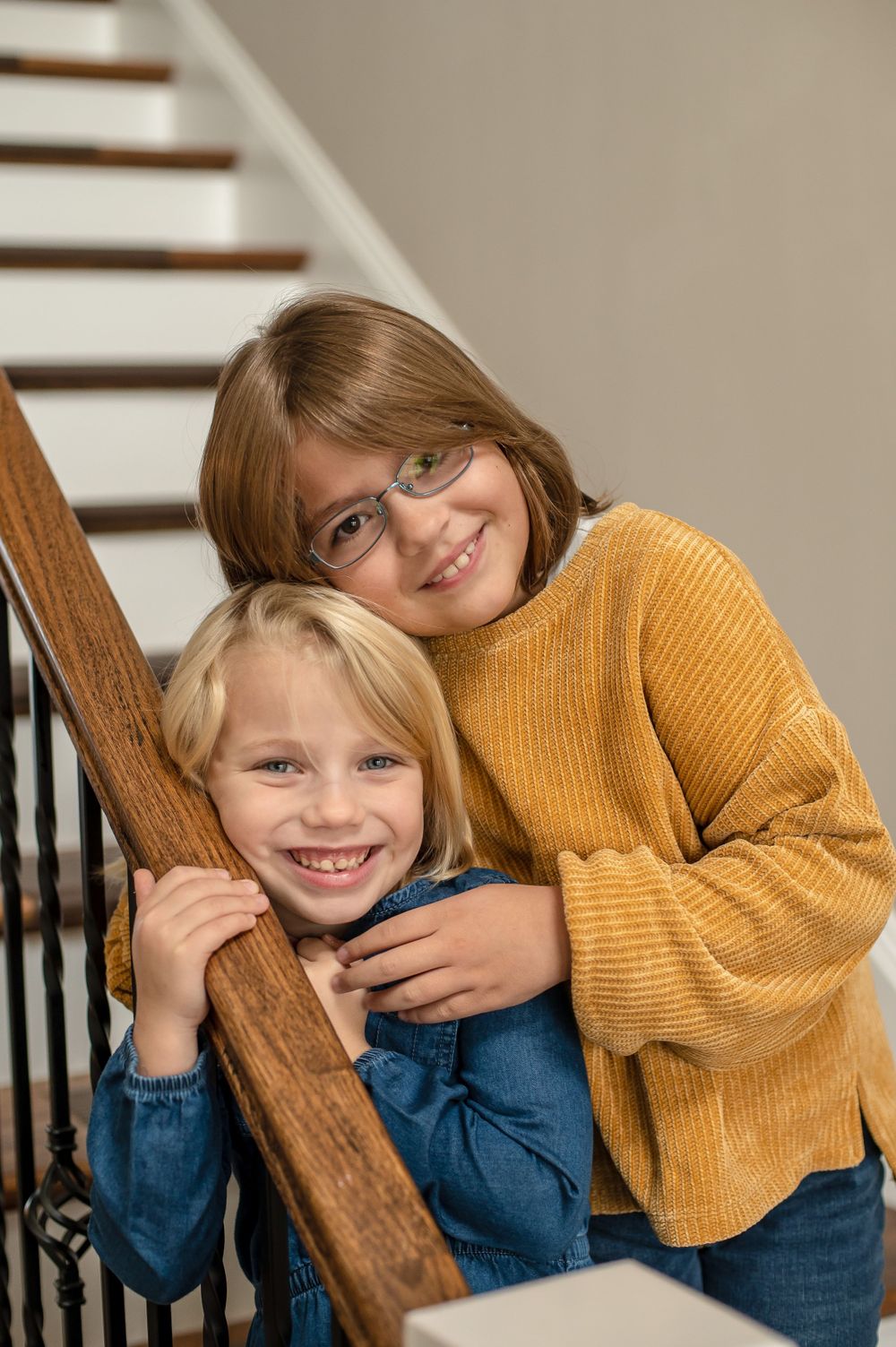 Two children share a sweet moment on wooden stairs with iron railing.