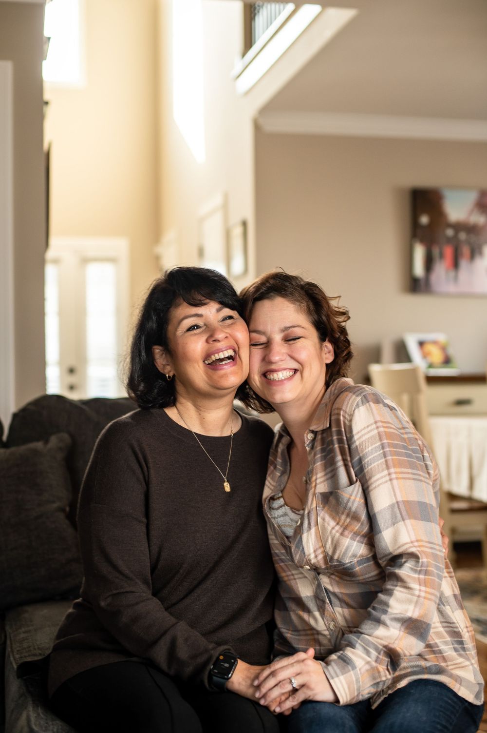 Two people sharing joyful laughter while sitting on dark couch in living room.