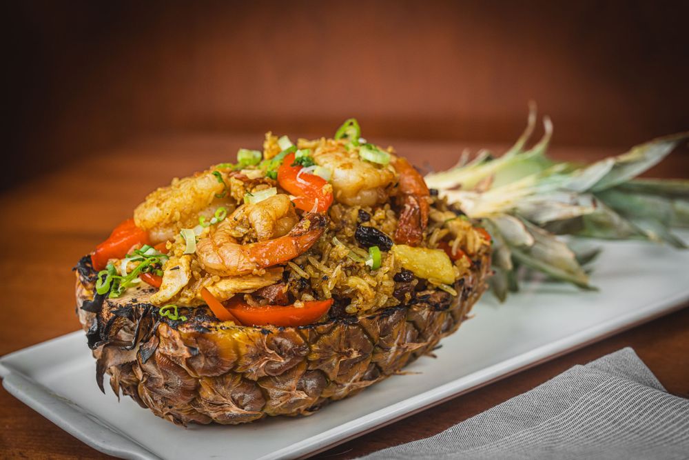 A hollowed pineapple filled with stir-fried shrimp, rice, and colorful vegetables on a white plate.