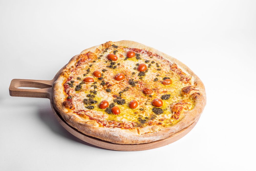 Margherita pizza with cherry tomatoes and melted cheese on a round wooden board.