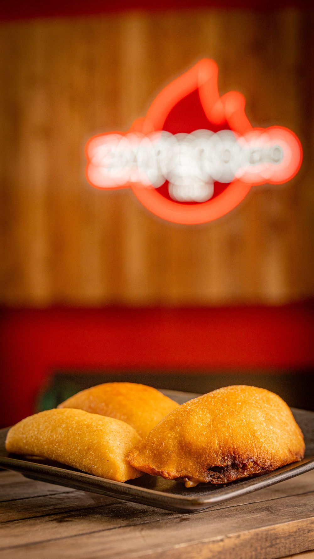 Two golden fried empanadas served on a black plate at Zaperoco restaurant.