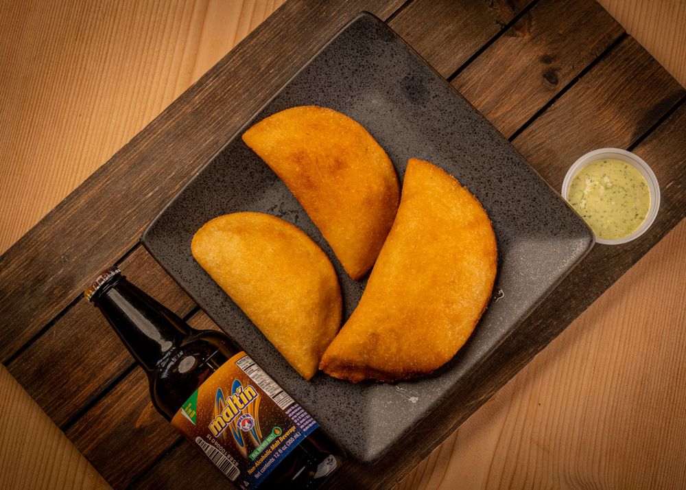 Three crispy fried empanadas with green dipping sauce and a beer bottle on wood.