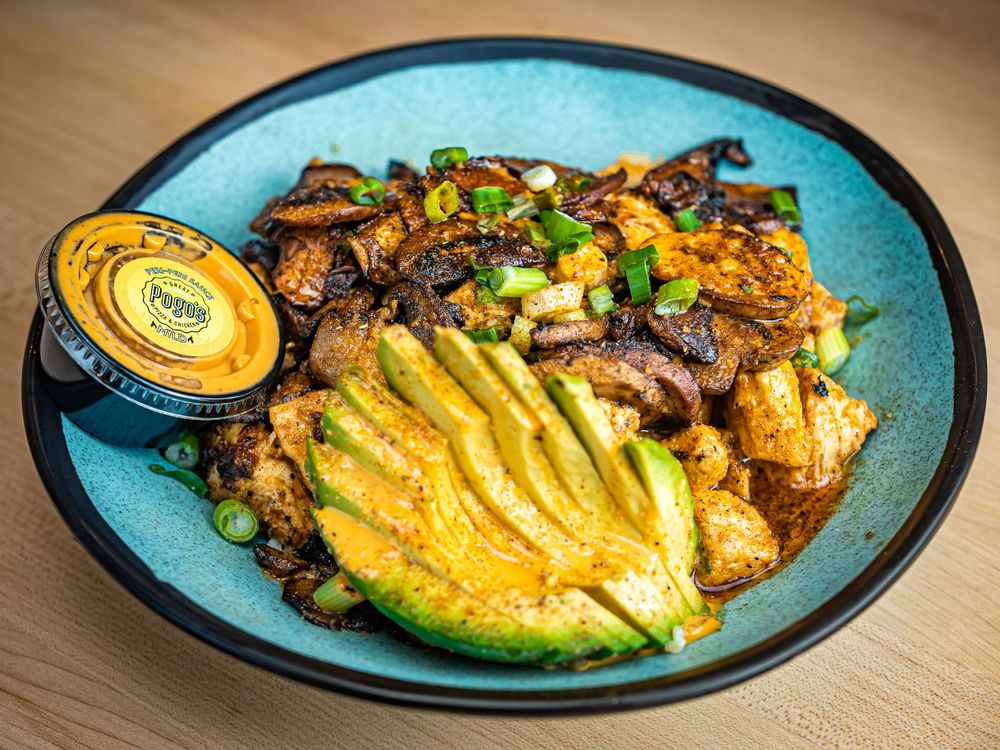 A blue bowl filled with sliced avocado, sauteed mushrooms, and rice topped with fresh green onions.