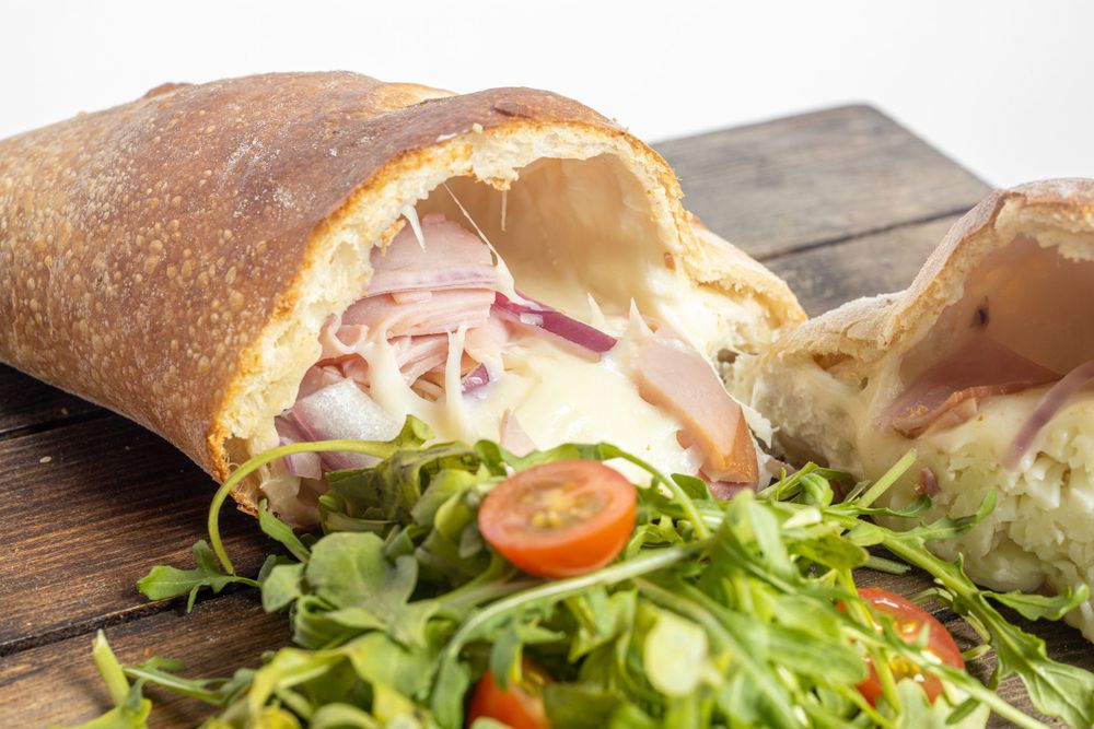 A sliced ciabatta sandwich filled with ham, melted cheese, and red onion served with fresh salad greens.
