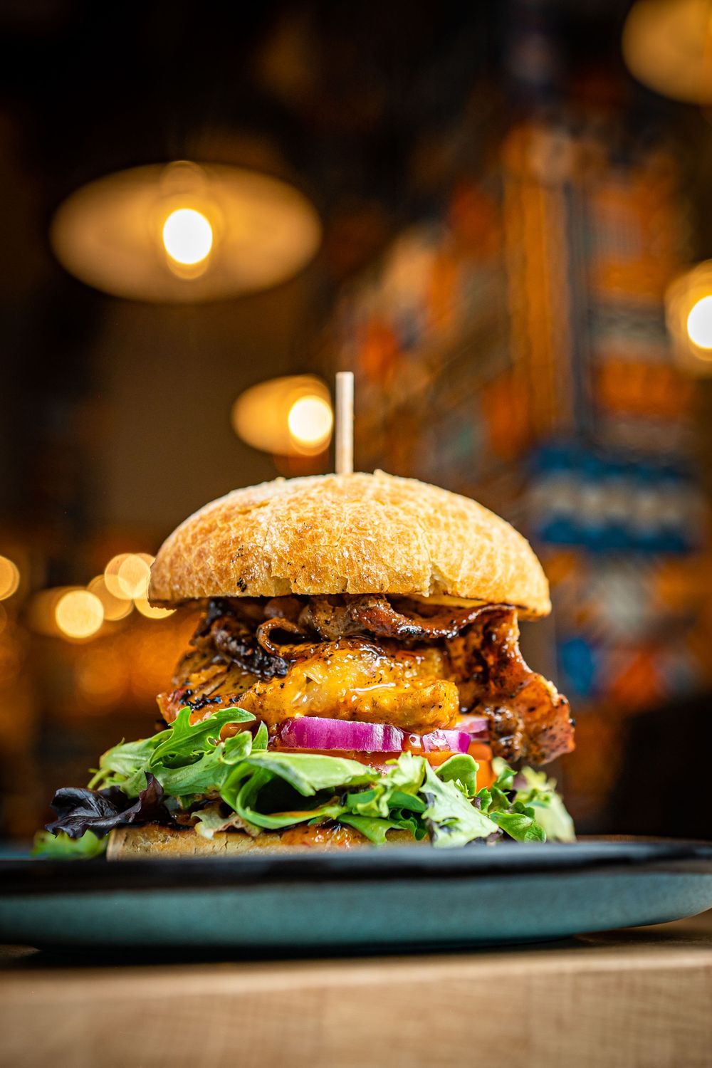 A tall gourmet burger with melted cheese, red onion, and fresh greens on a blue plate.