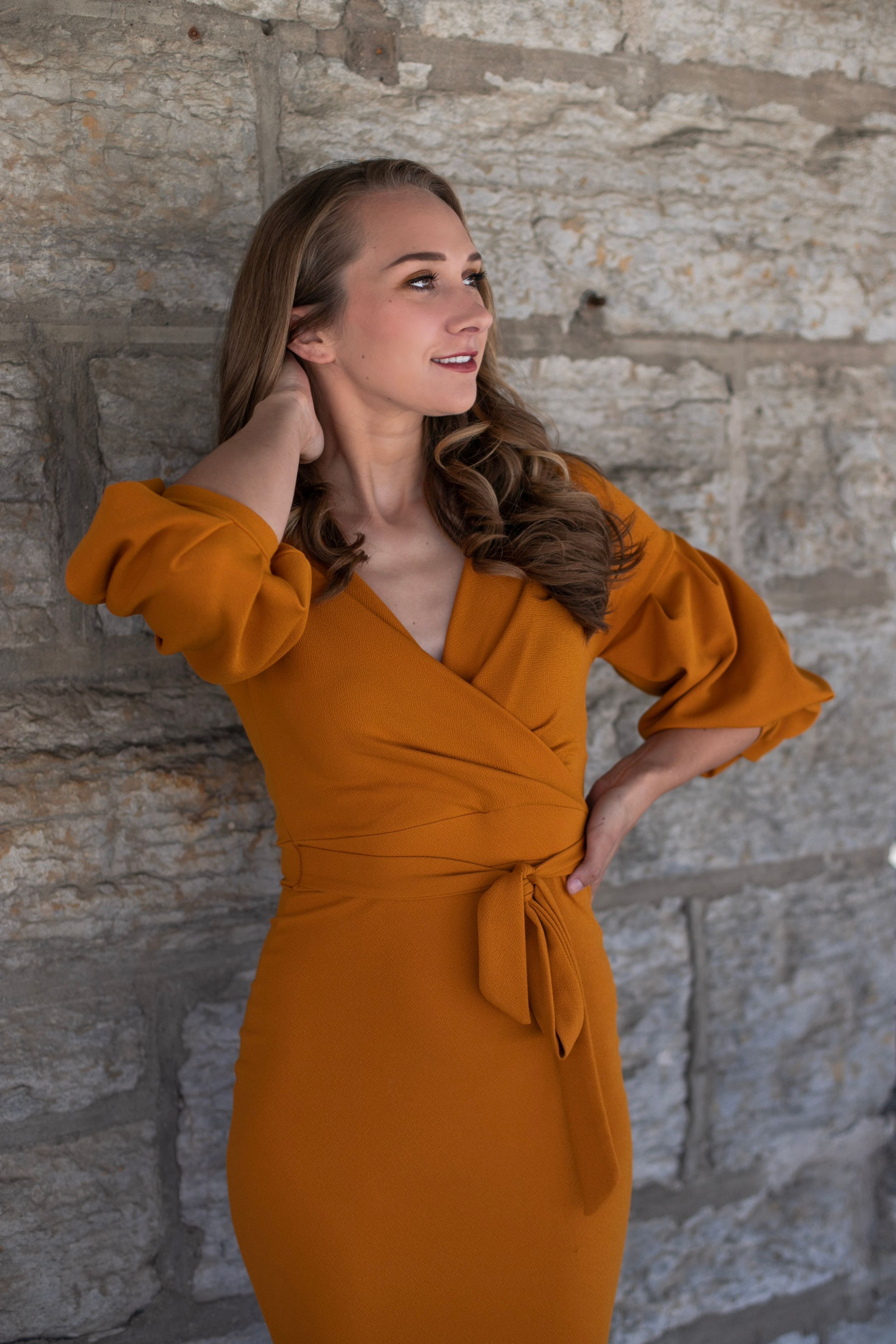 An orange wrap dress with dramatic puff sleeves photographed against a limestone wall.