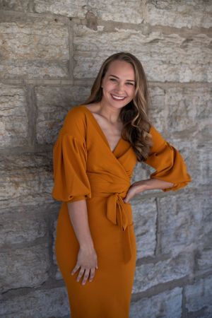 A feminine orange wrap dress with statement sleeves posed against a textured stone wall.