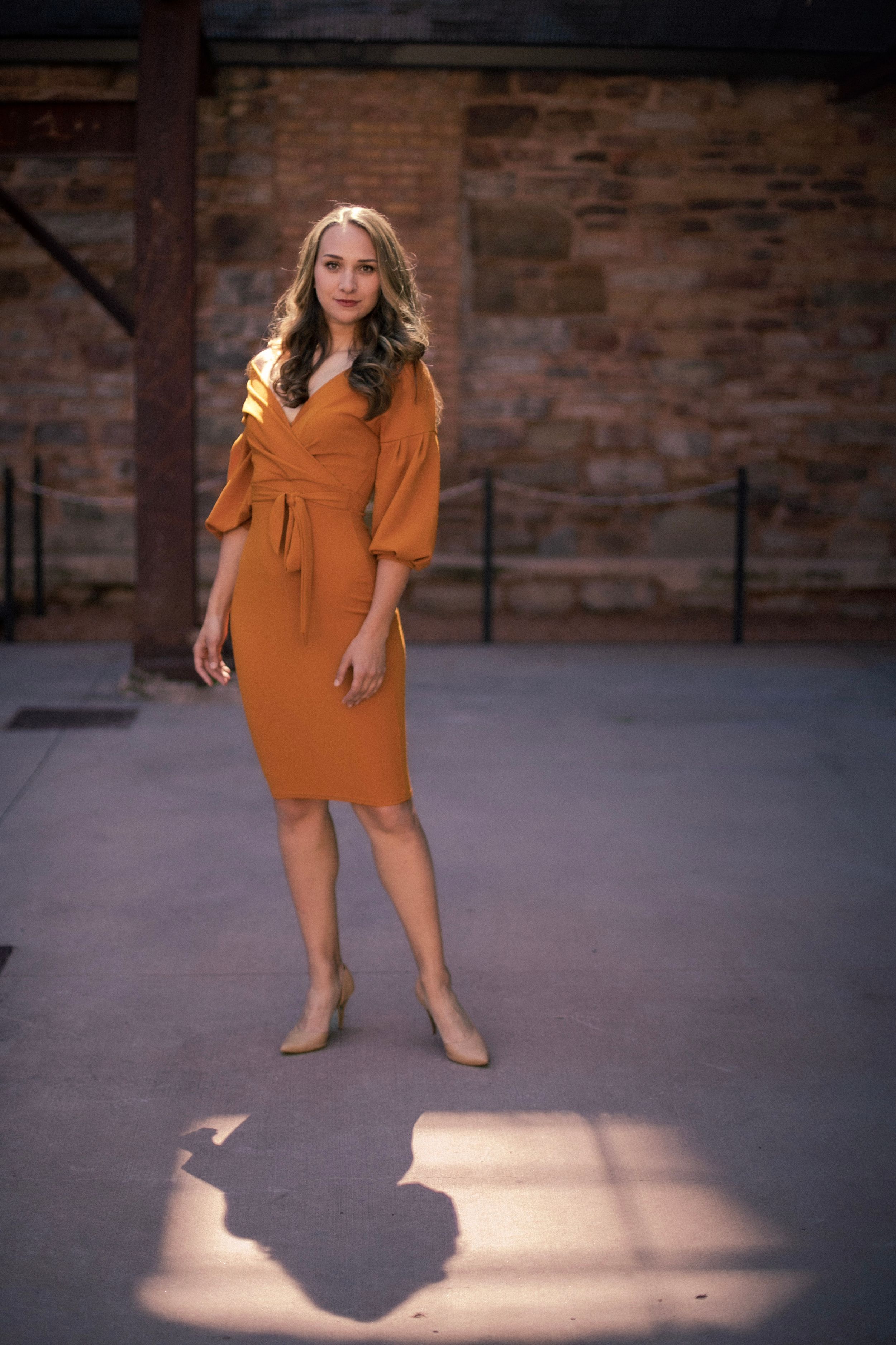 An orange knee-length dress with balloon sleeves shown in a dramatic shadow play setting.