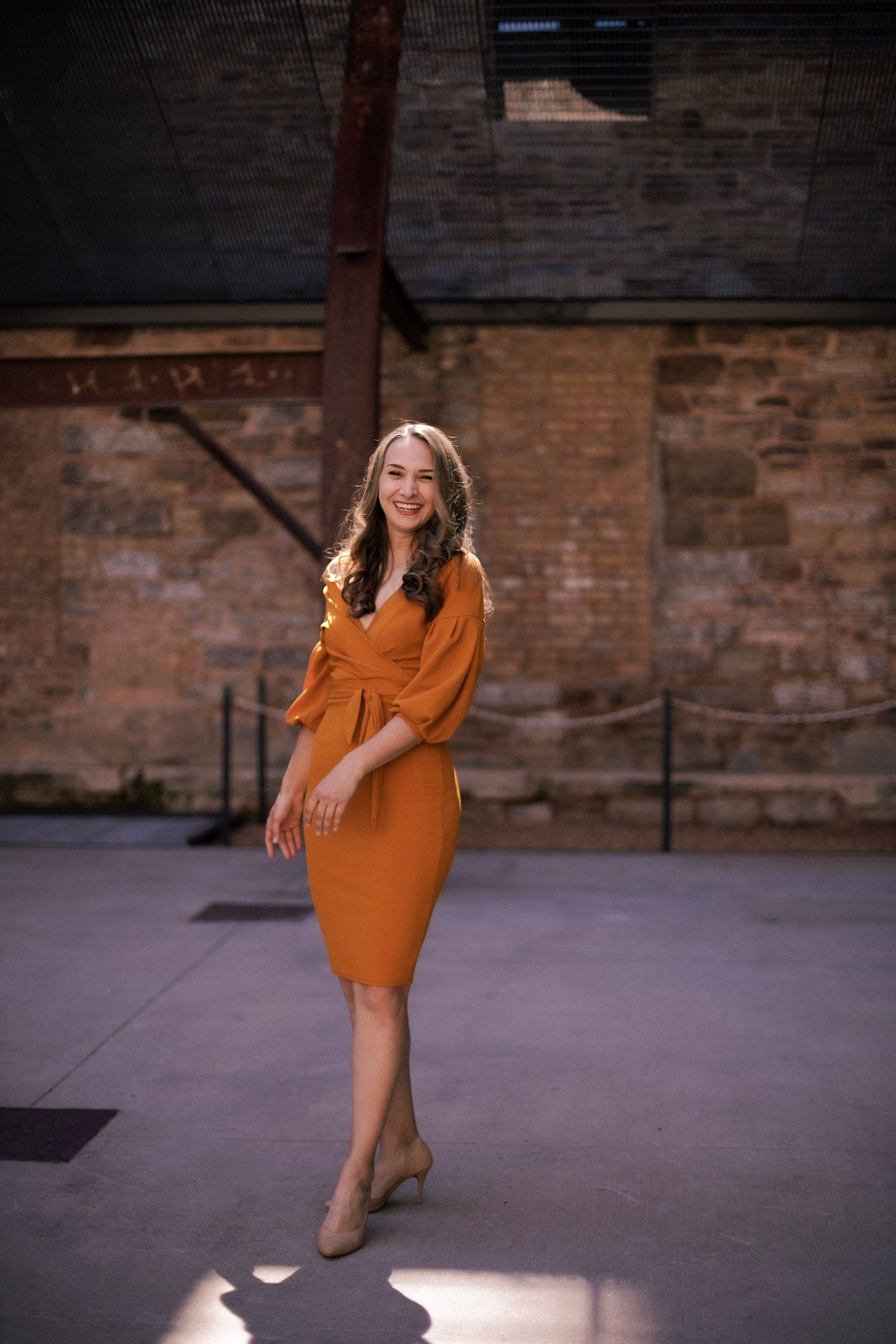 A form-fitting orange dress captured in dramatic lighting against a brick wall backdrop.