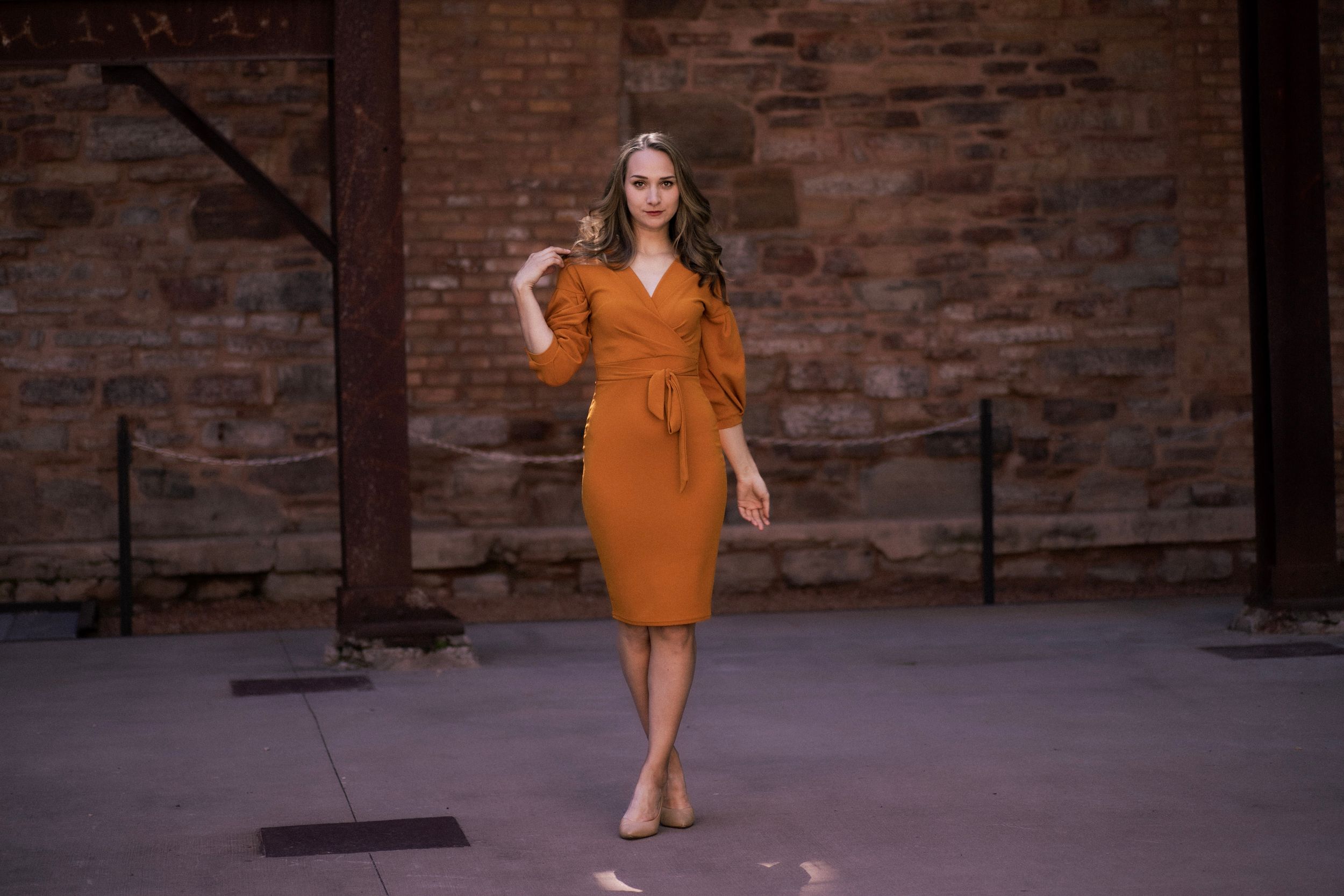 A structured orange wrap dress with voluminous sleeves photographed in an urban setting.