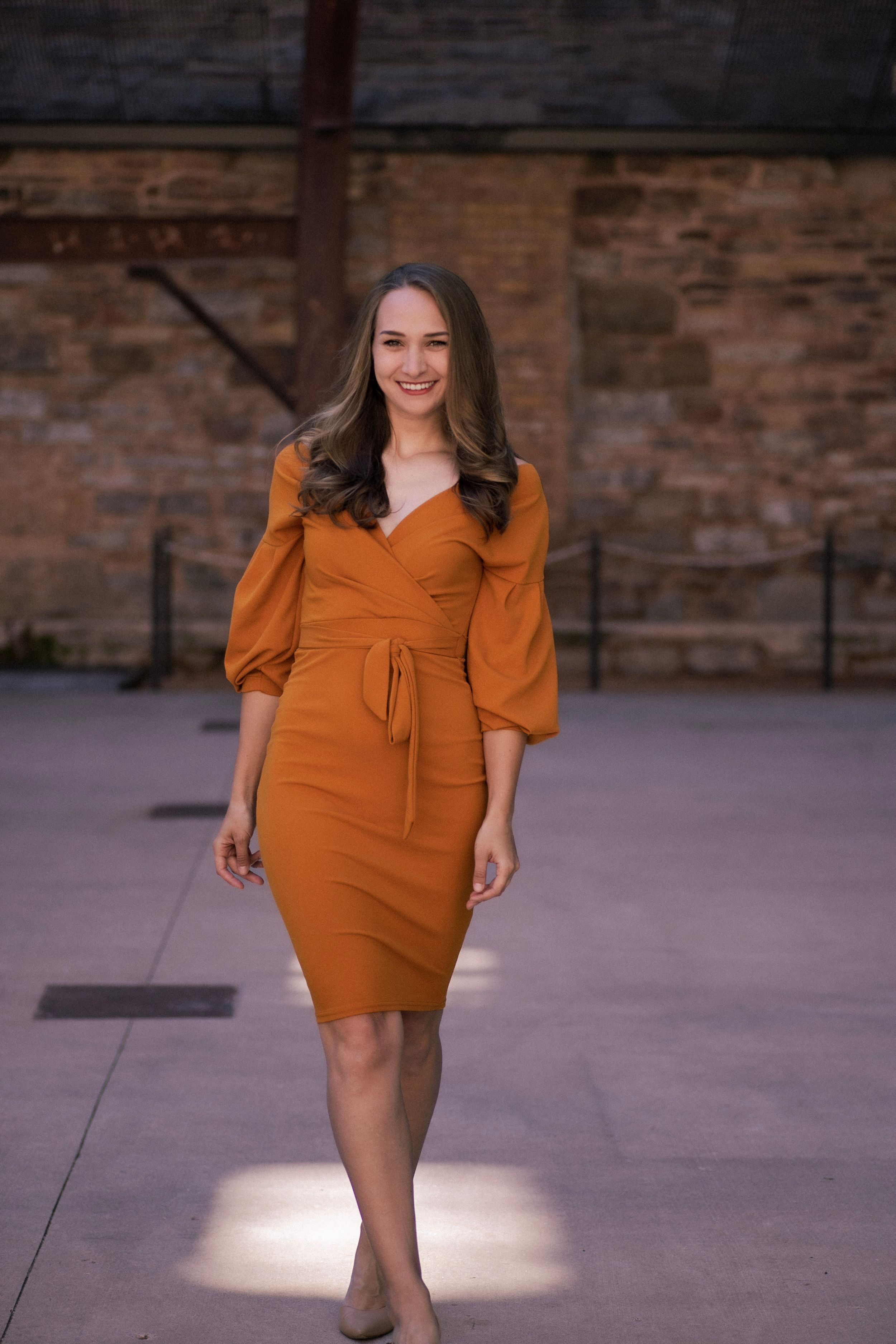 A fitted orange midi dress with three-quarter puff sleeves styled against brick architecture.