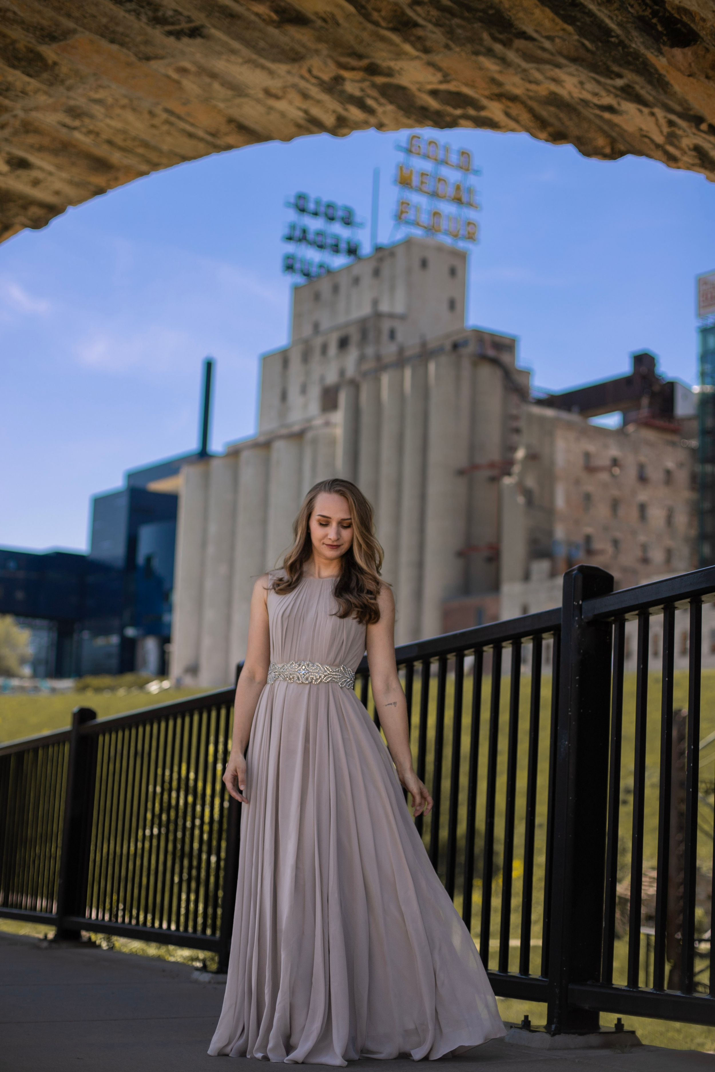 An elegant floor-length gray gown photographed in front of an industrial grain silo building.