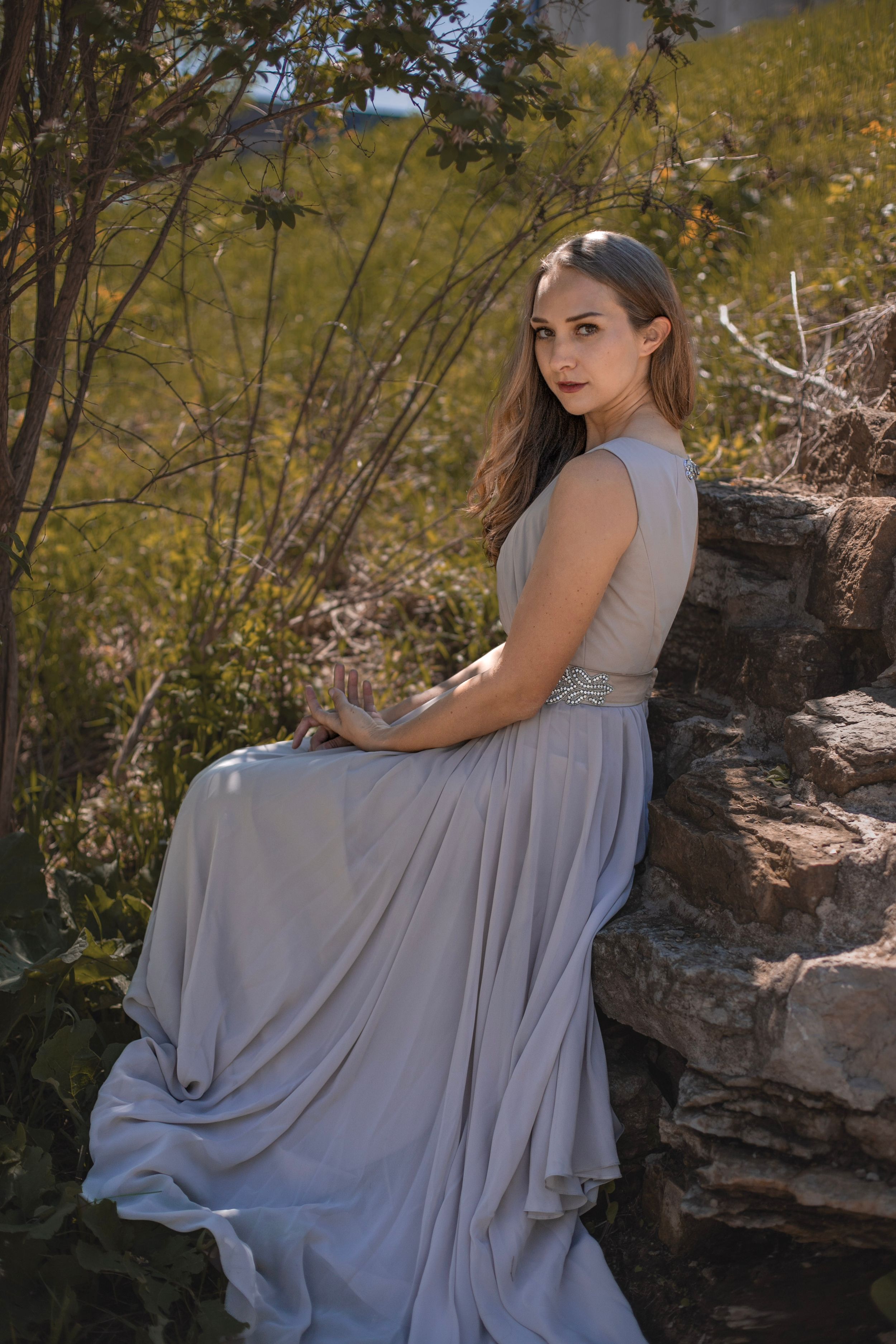 A person in a flowing gray dress poses on rocky terrain with autumn foliage.