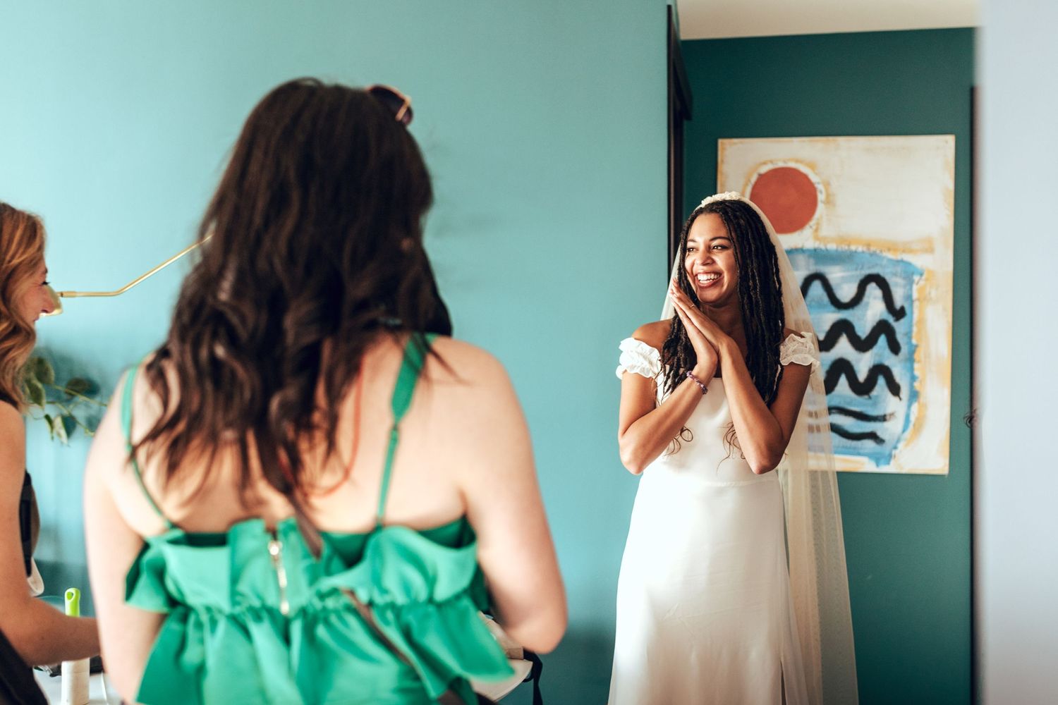 People in green and white dresses interacting in a room with turquoise walls.