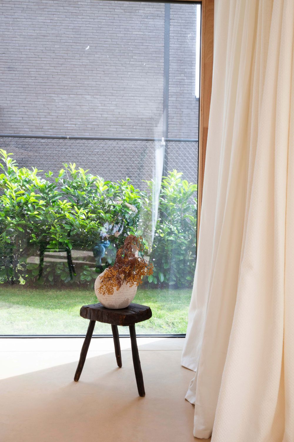 Modern living room with white curtains and window overlooking green garden space.