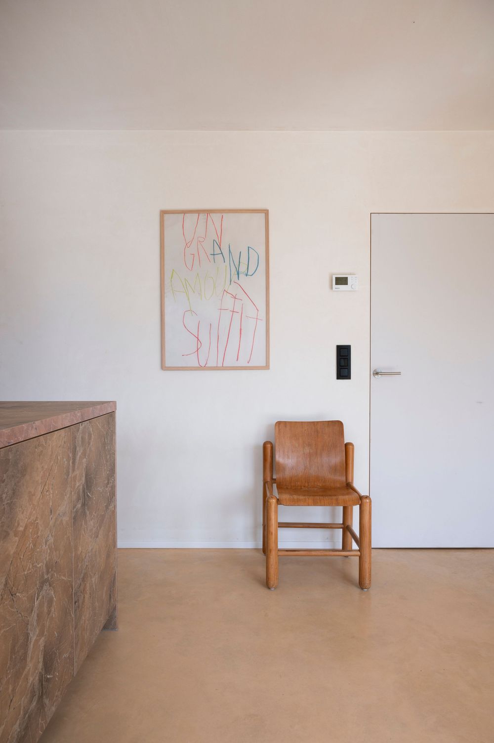 Minimalist room interior with wooden chair and framed artwork on white walls.