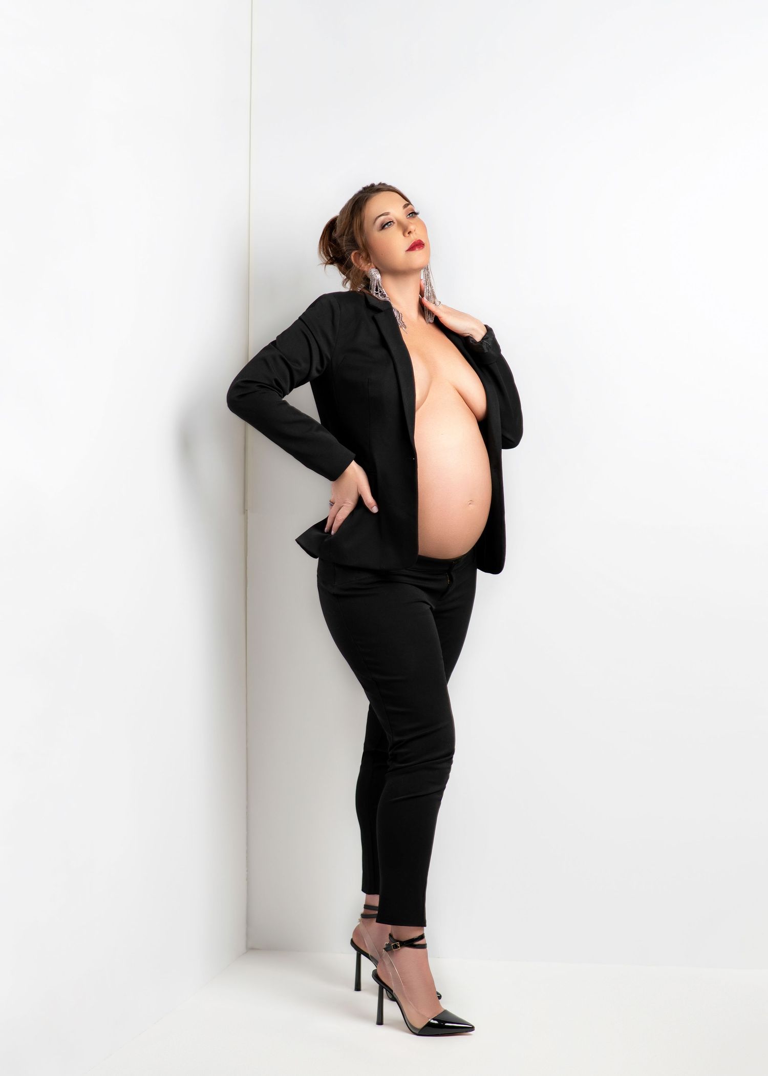 a woman looks up fiercely with a hand on her clavicle while showing her baby bump under a black suit jacket