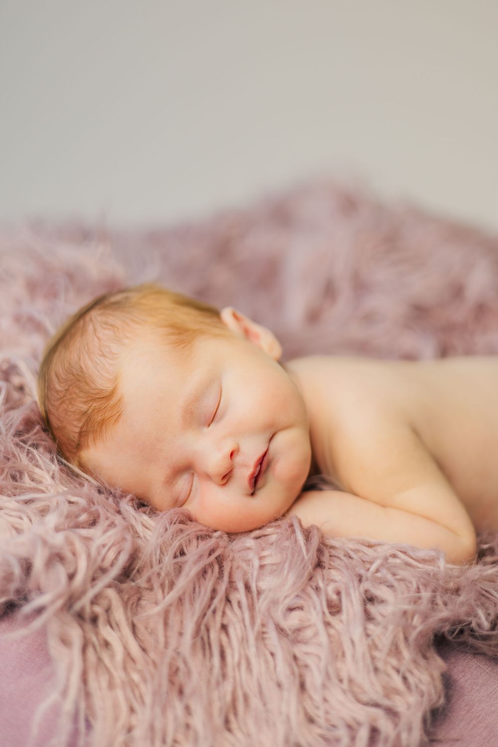 Peaceful newborn sleeping on soft pink fur backdrop in natural light.
