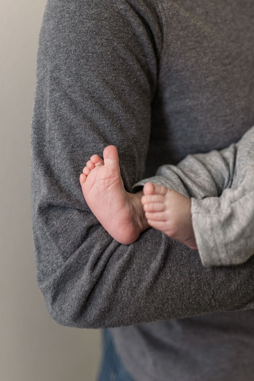 A tiny baby foot rests against a person wearing a gray sweater sleeve.