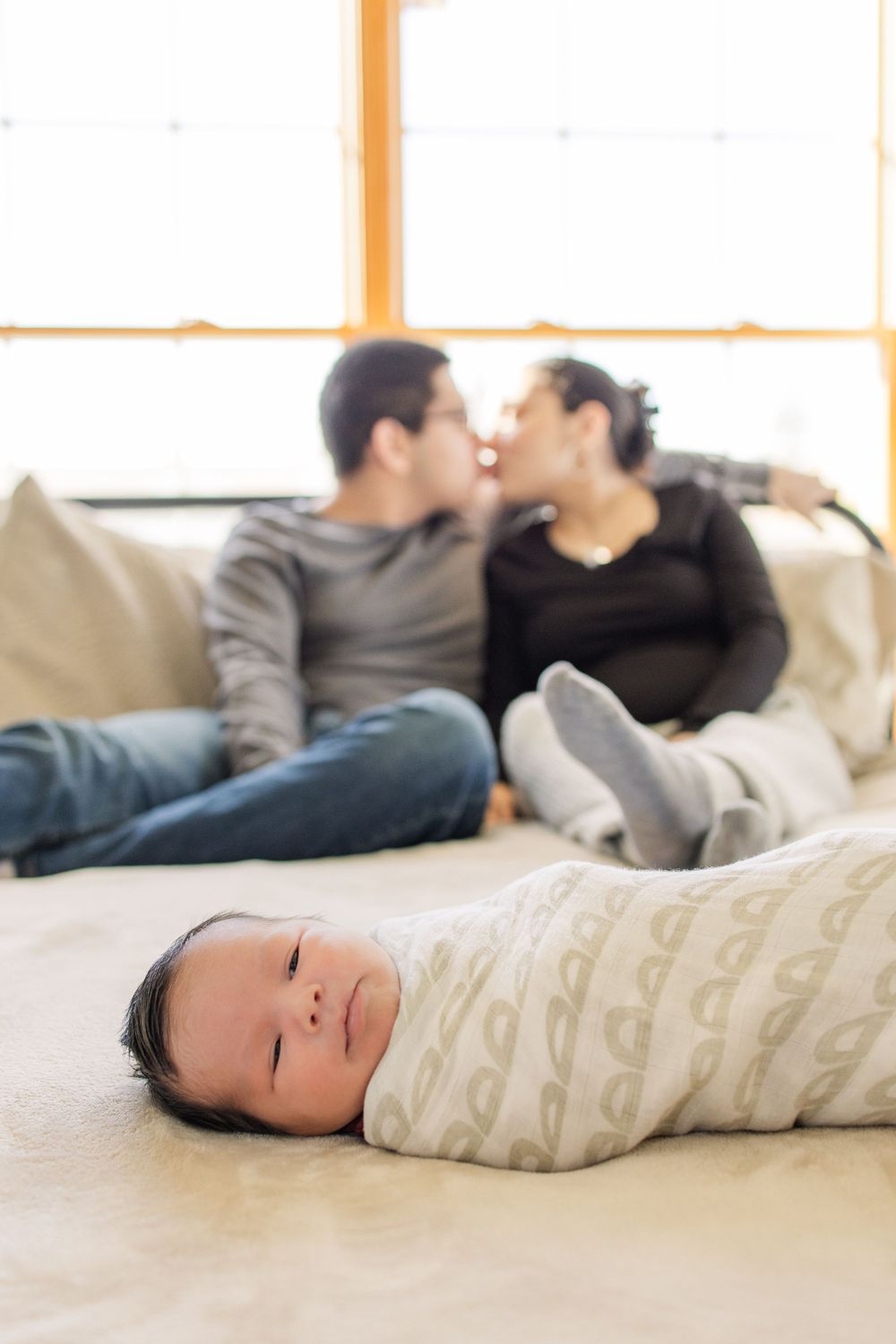 Sleeping baby in foreground with couple sharing intimate moment on couch in background.
