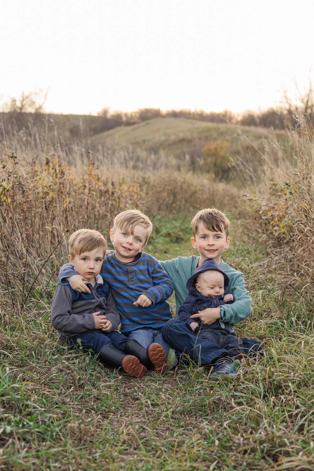 Four young children sit together in tall grass on an autumn hillside.