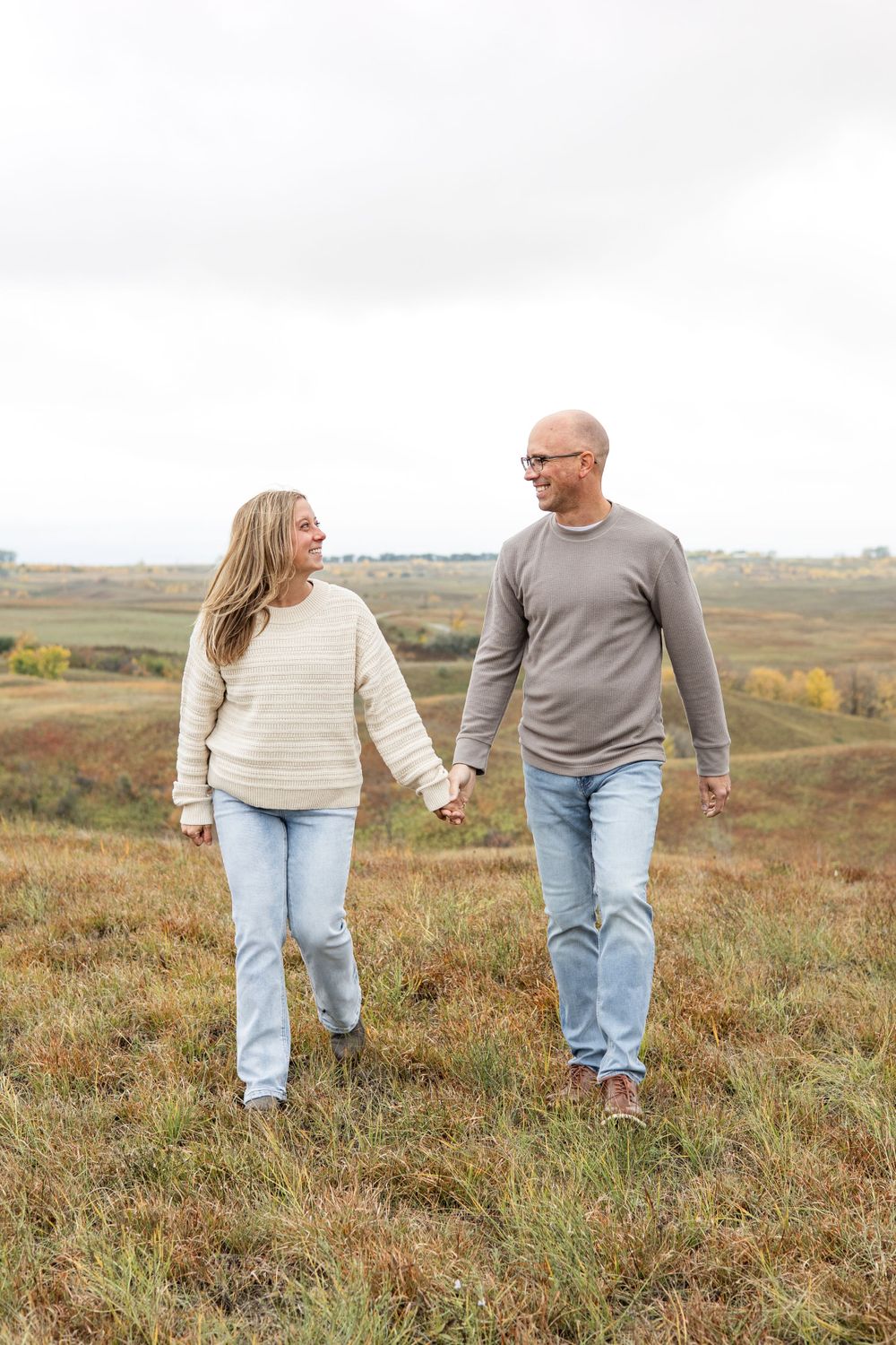 A couple holds hands while walking together on an autumn hillside.