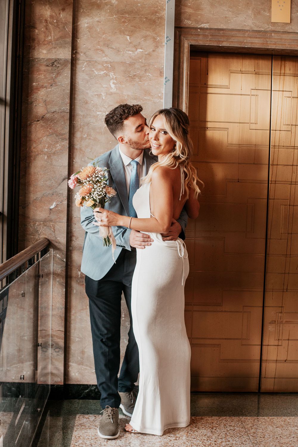 Elegant wedding couple embracing in formal attire with floral bouquet.