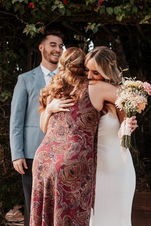 Joyful embrace between wedding attendees with floral bouquet.