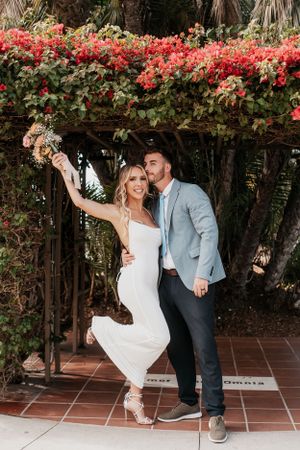 Playful wedding couple dancing on terracotta tiles under flowering vines.