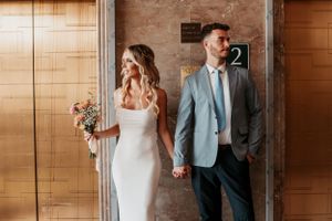 Newlywed couple in formal attire standing in modern hallway.
