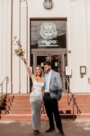 Newlywed couple posing outside a historic building with red brick steps and an ornate entrance.