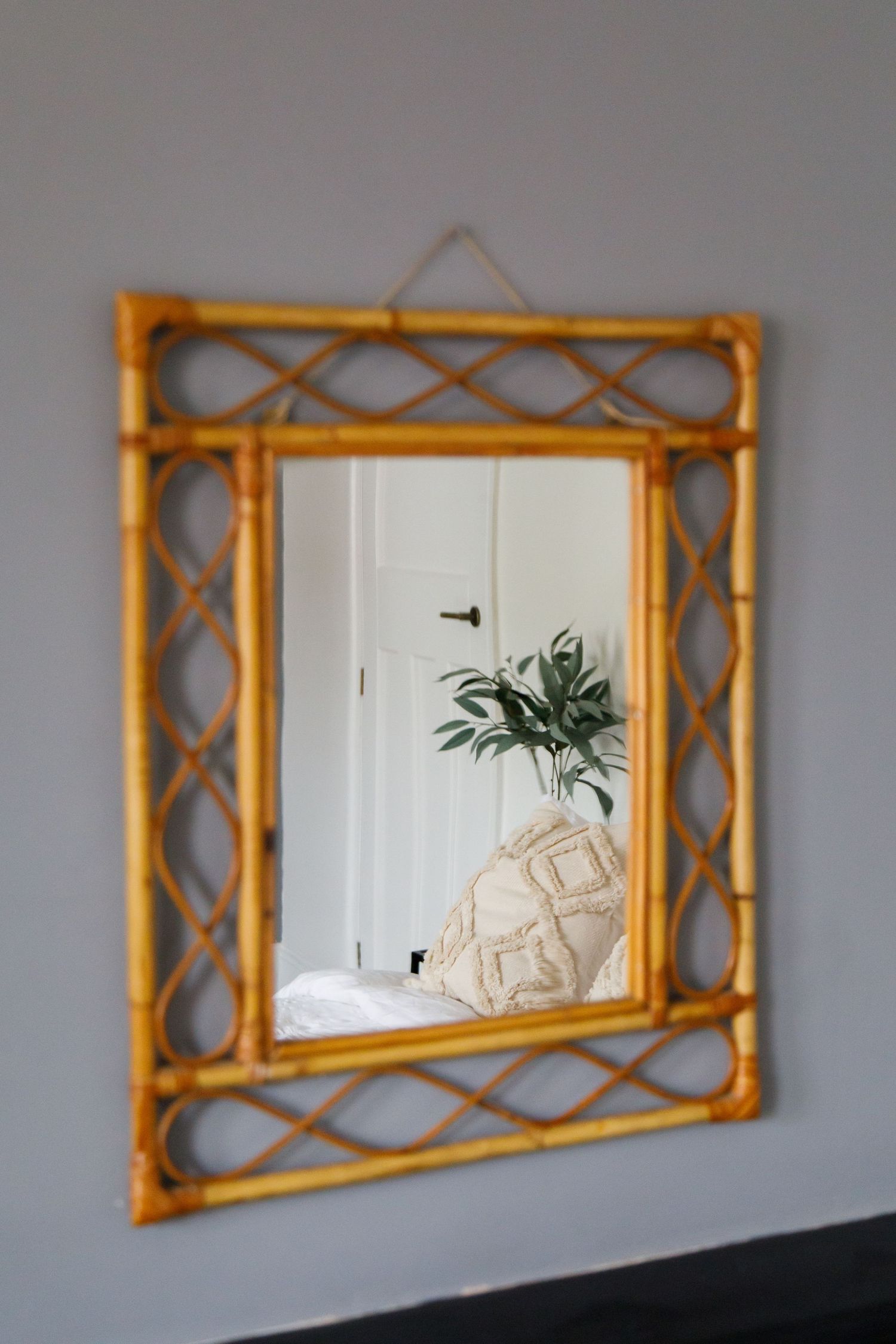 Bamboo-framed mirror reflecting interior decor and houseplant in white room taken during an interiors/lifestyle photoshoot.